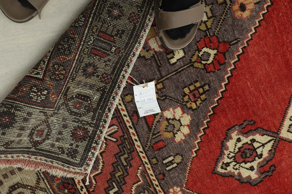 Overhead view of the rug with a label and part of a shoe, indicating scale and the rug's condition.