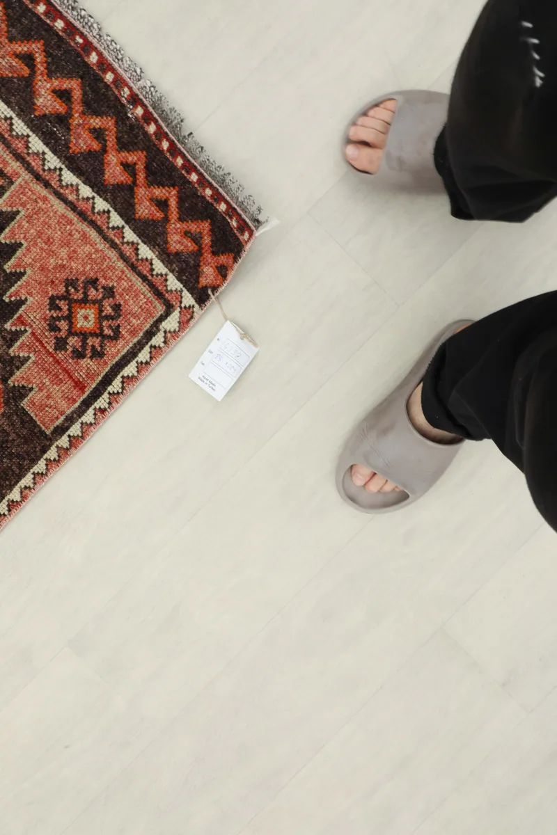 Overhead view of the Rose Orange Geometric Anatolian Runner's end with feet for scale.