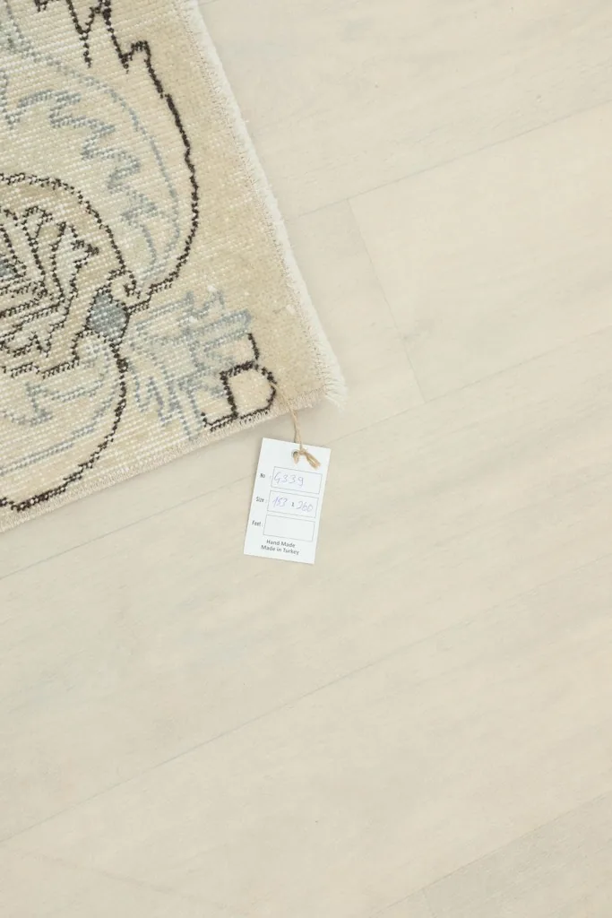 Rug corner with a tag indicating its origin and material, resting on a light wood floor