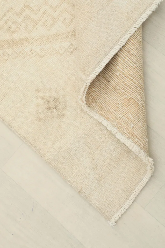 Corner of the rug folded to reveal the cotton foundation and the reverse side of the hand-knotted construction.
