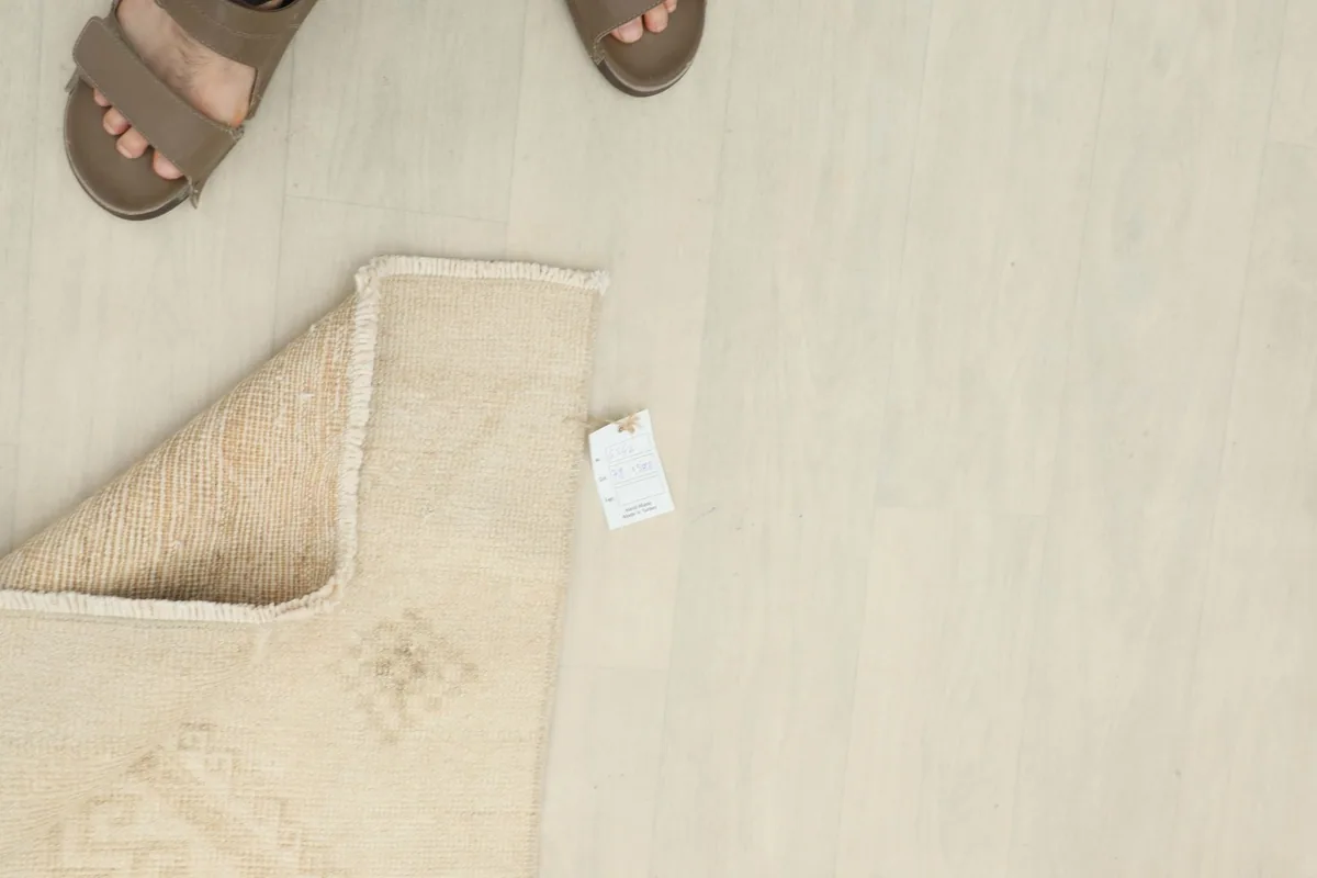 Overhead view of the rug's corner with a size tag and feet in sandals, indicating scale.