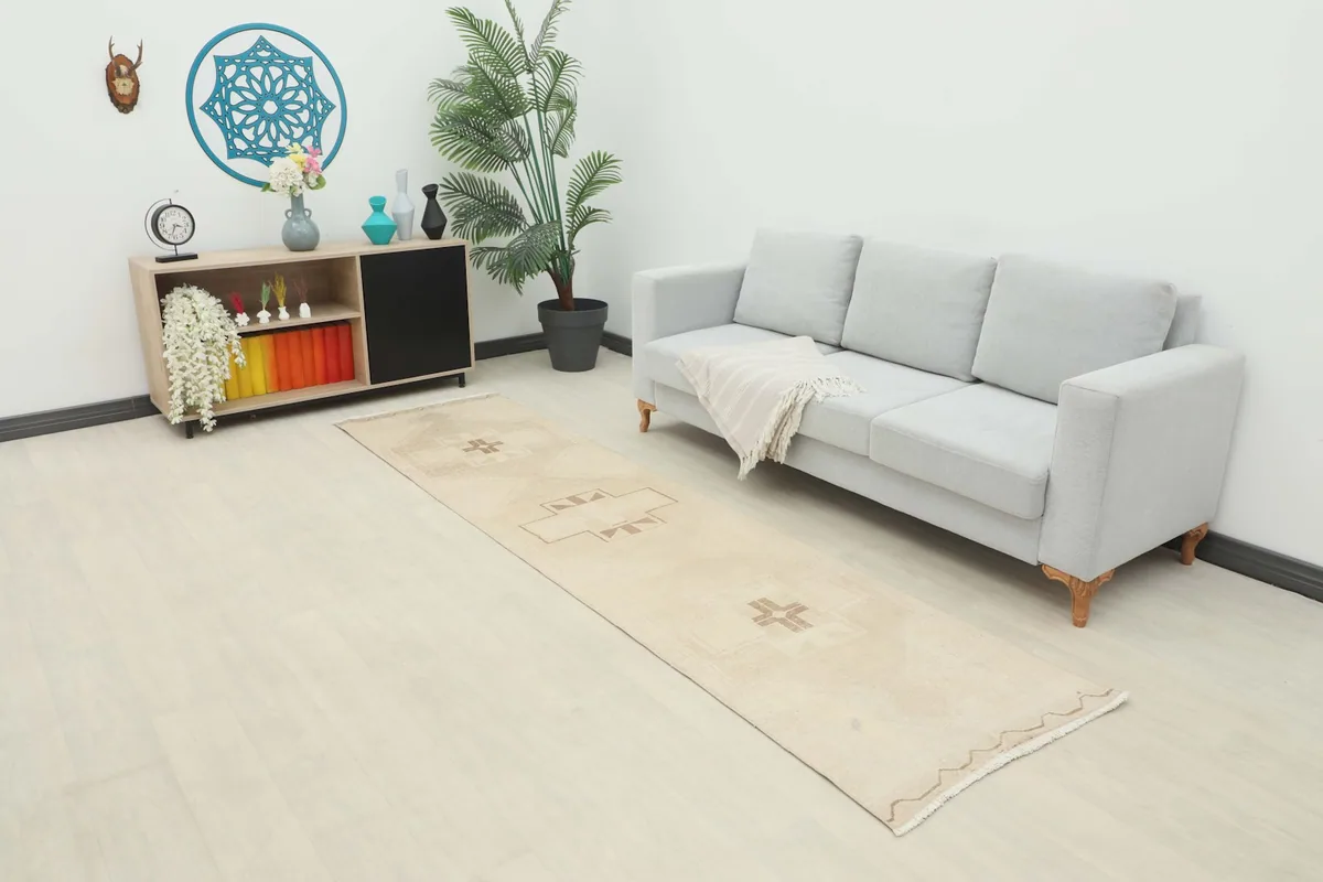Ivory beige runner rug in a modern living space, extending from a cabinet past a light gray sofa.
