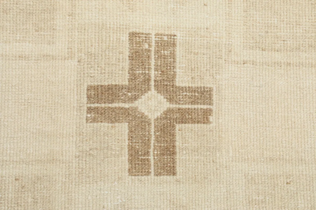 Detailed view of a cross-like geometric design in brown, highlighting the hand-knotted texture.
