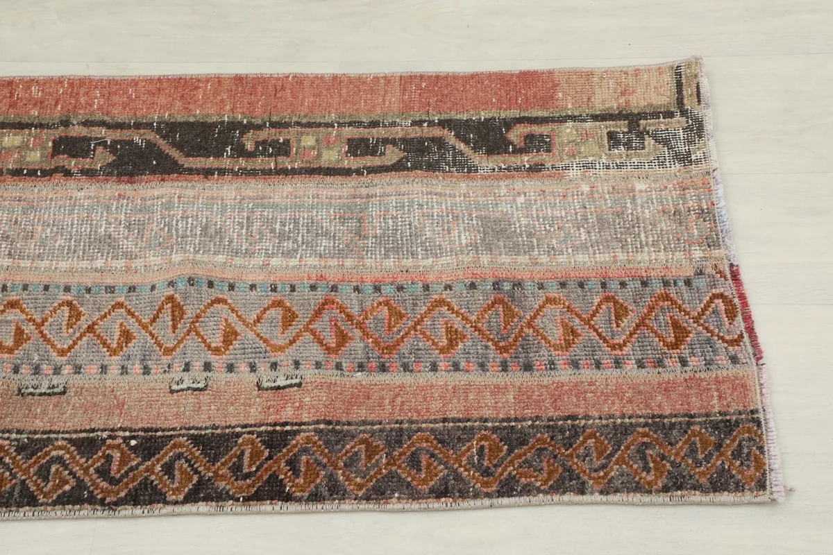 Close-up of the rug's end, showing striped patterns and muted rose, gray, and black colors