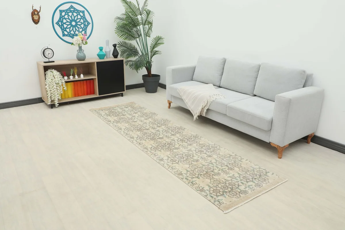 Vintage ivory runner rug displayed in a modern living room setting with a light gray sofa and wooden cabinet.