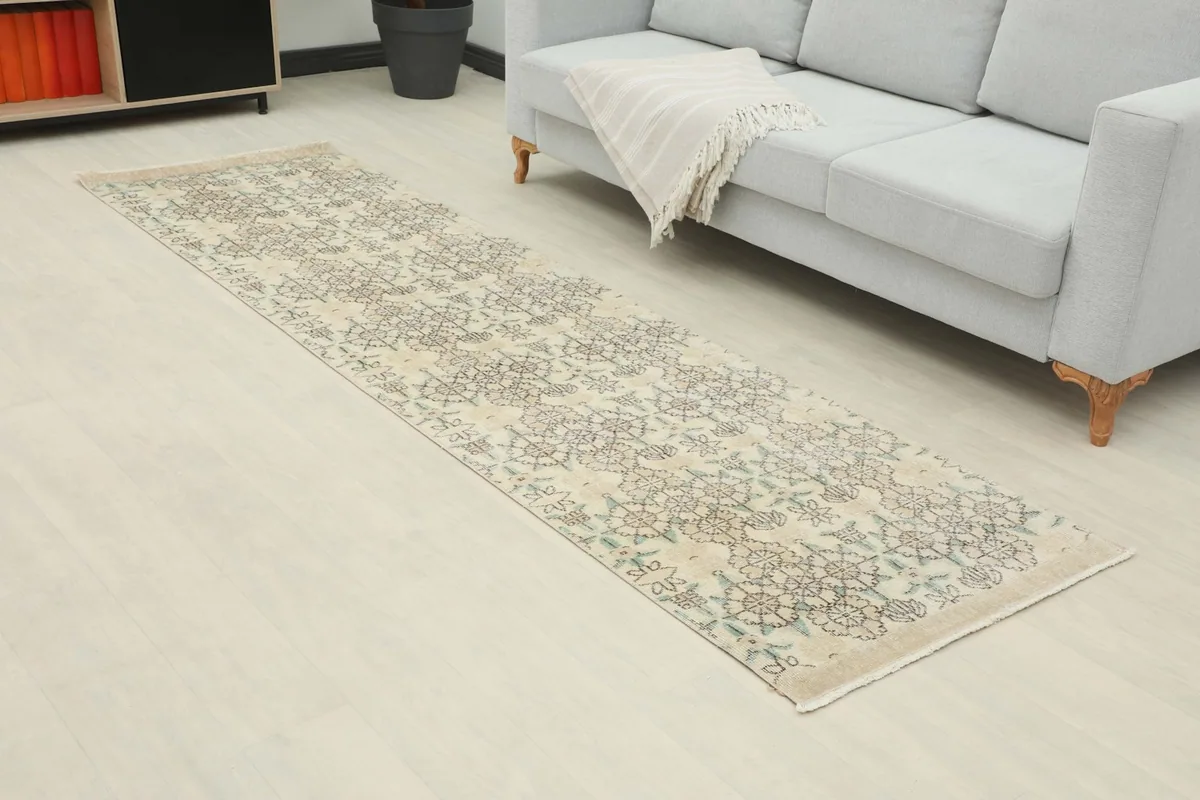 Angle view of the ivory runner rug in a room, showing its length and geometric pattern next to a sofa.