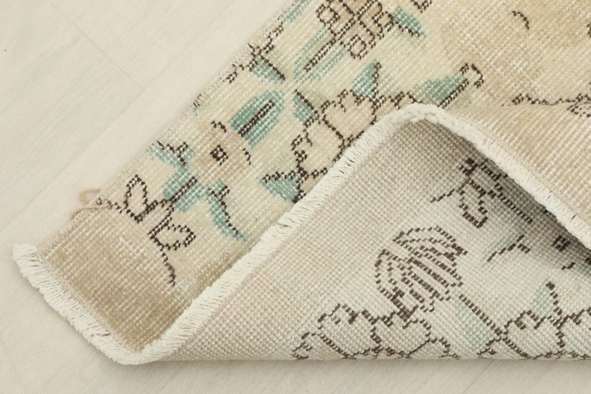 View of the rug's corner folded to show the low wool pile and the cotton foundation underneath.