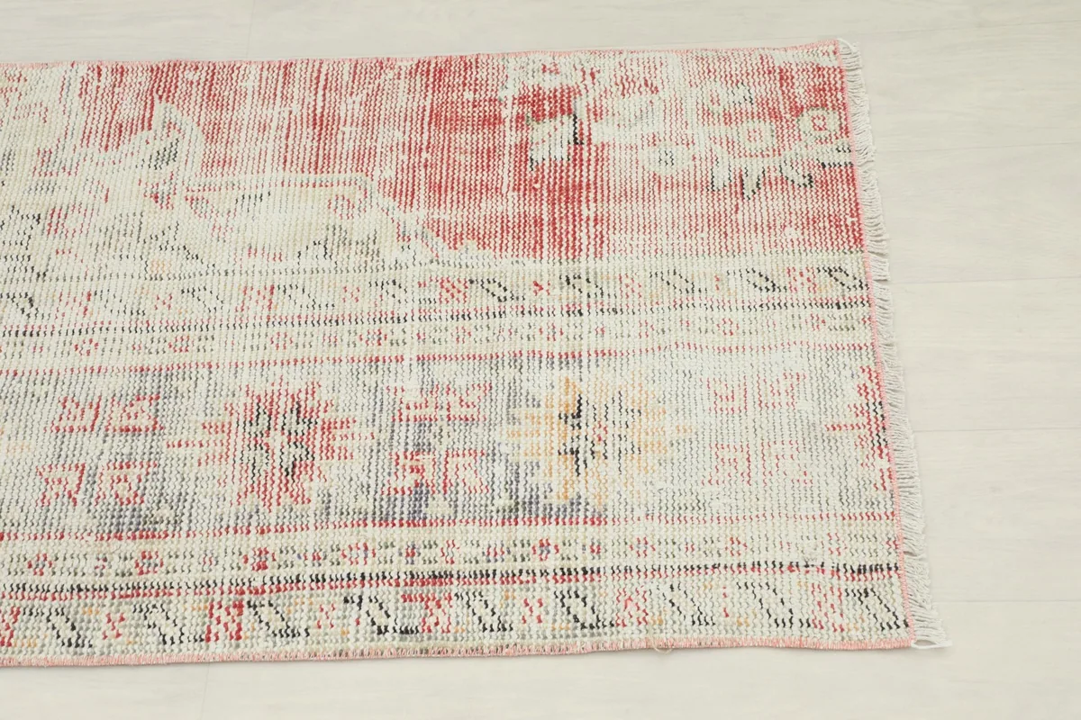 Close-up of the upper section of the rug, showing faded red and cream colors with geometric motifs.