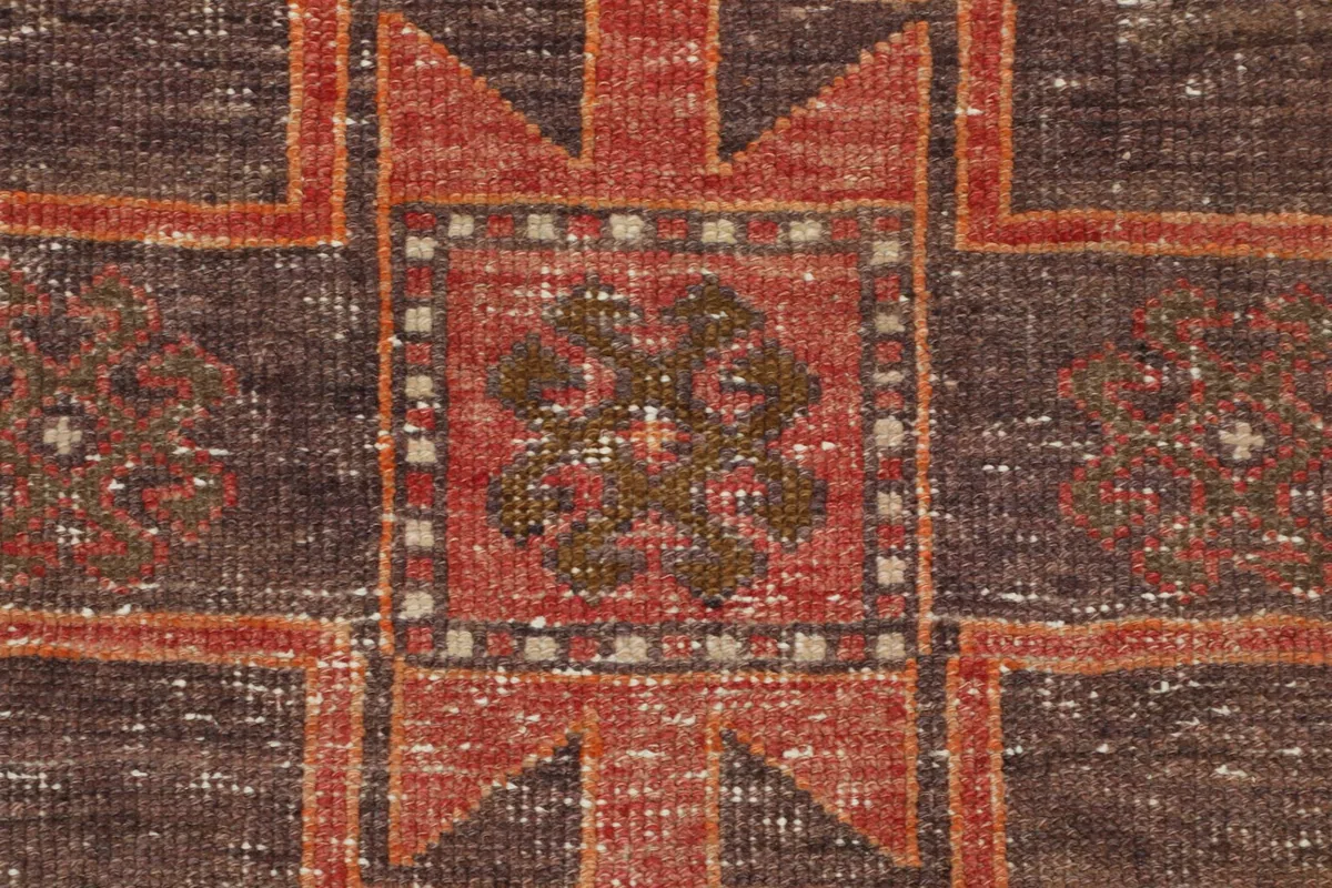 Extreme close-up of the hand-knotted wool pile, showing the intricate geometric design in brown, rust, and beige.