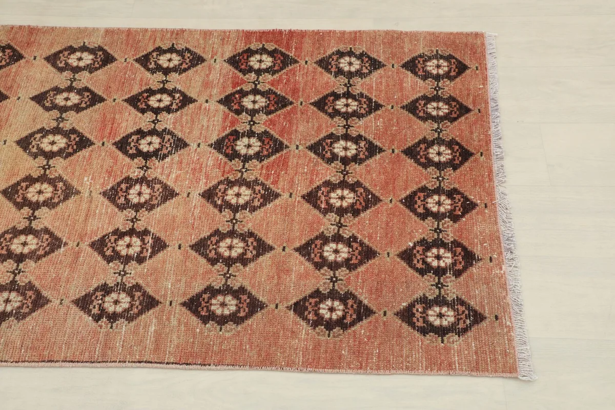 Close-up of the rug's end, showing the rust field and dark brown geometric diamond patterns