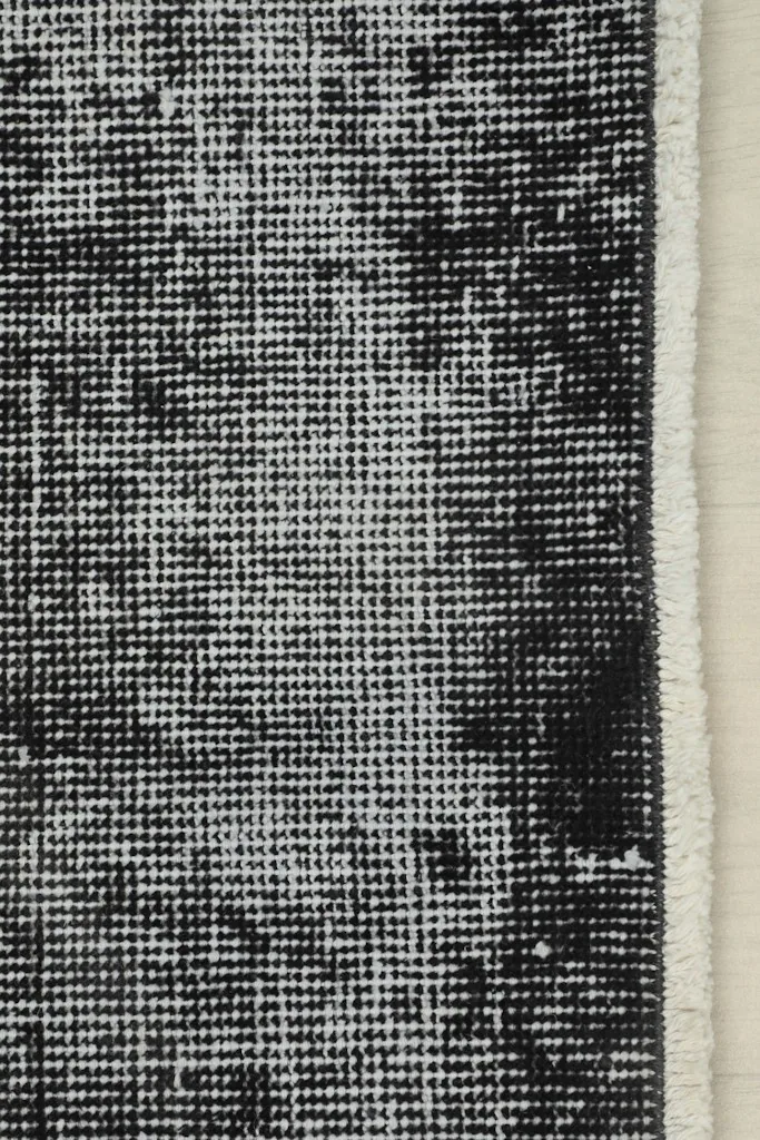 Close view of the rug's edge, highlighting the distressed charcoal and gray patterns and the natural wear.