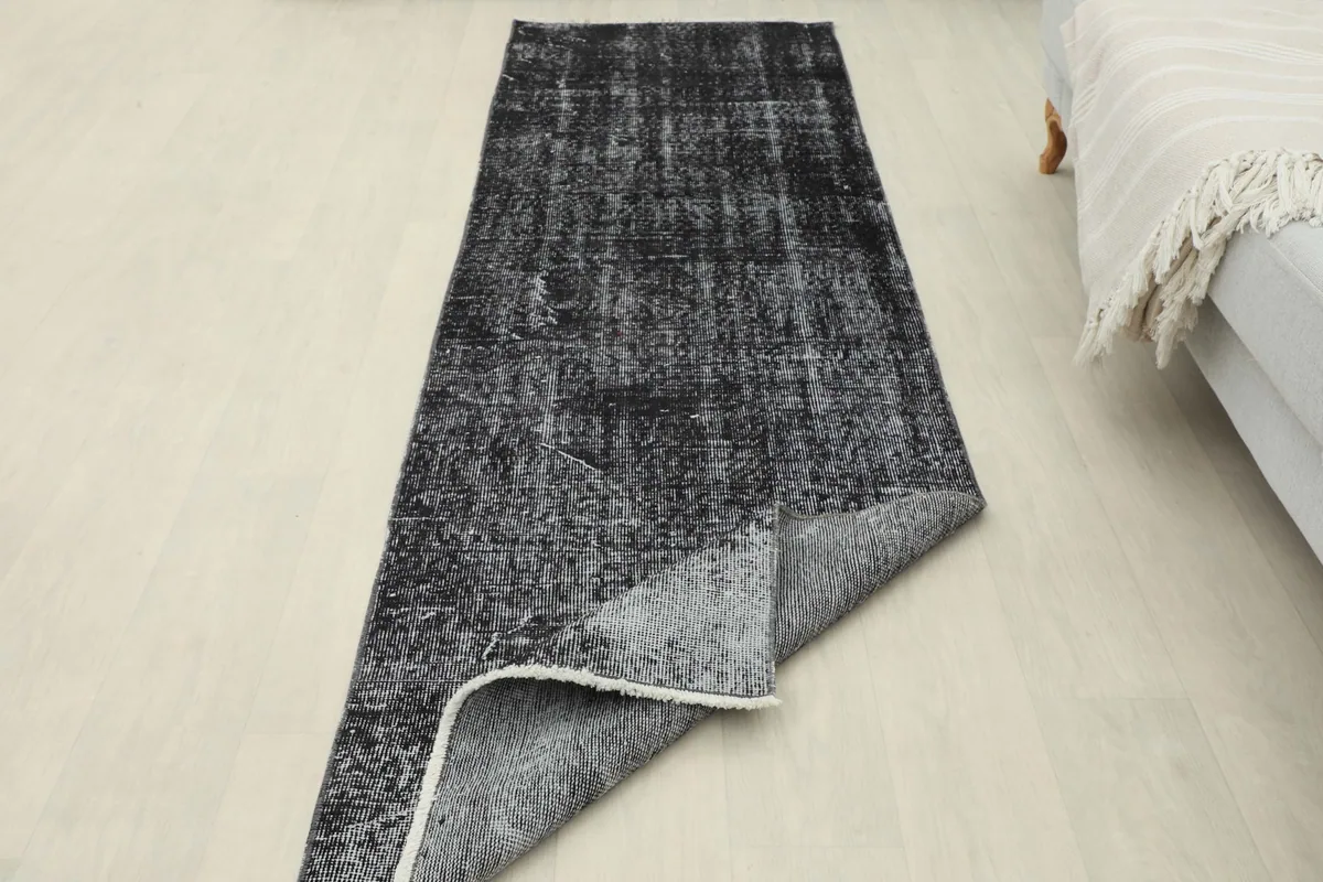 The rug partially folded back to show both the pile and the cotton foundation, illustrating its construction.