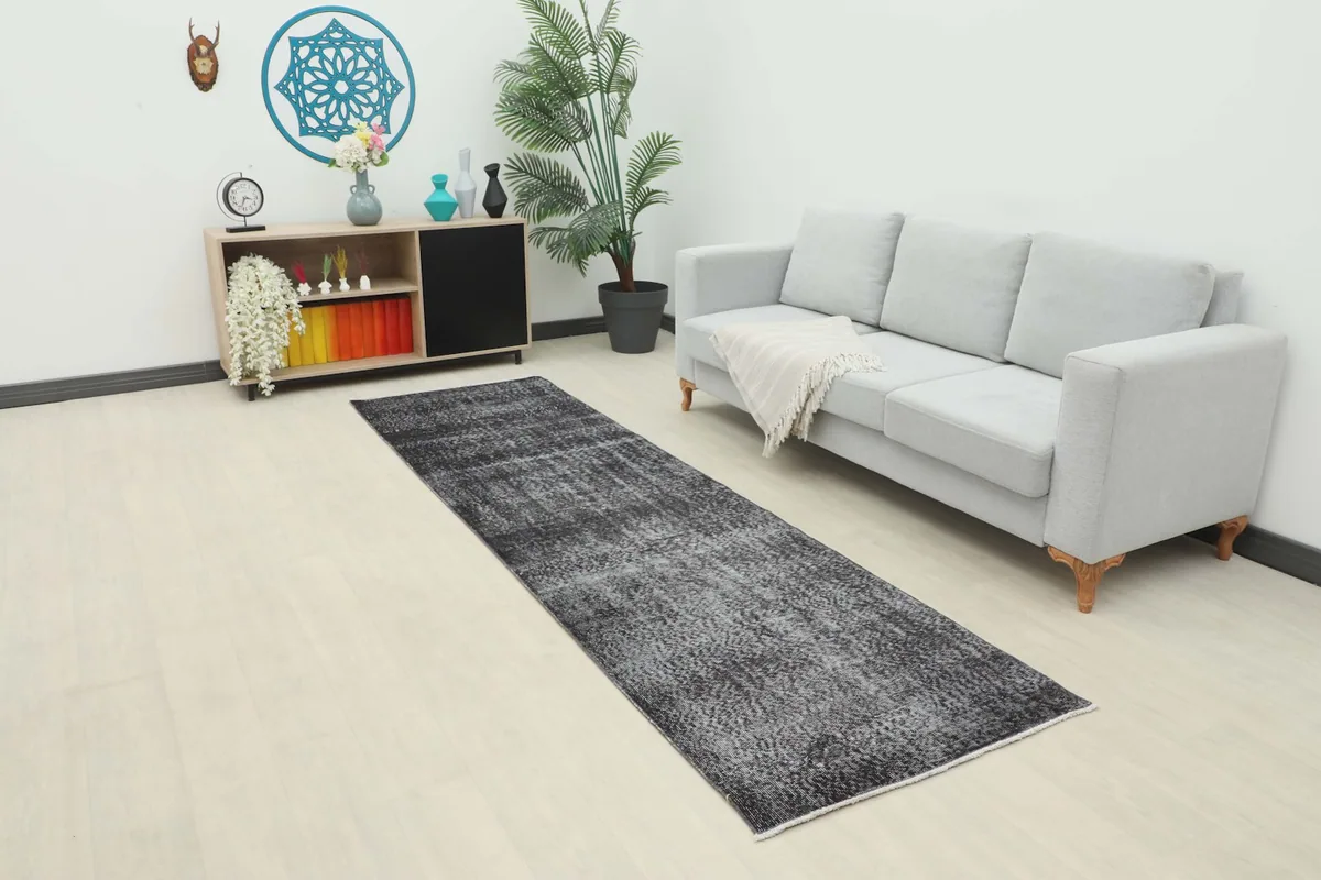 Vintage charcoal runner rug displayed in a modern room setting with a light gray sofa and wooden cabinet.