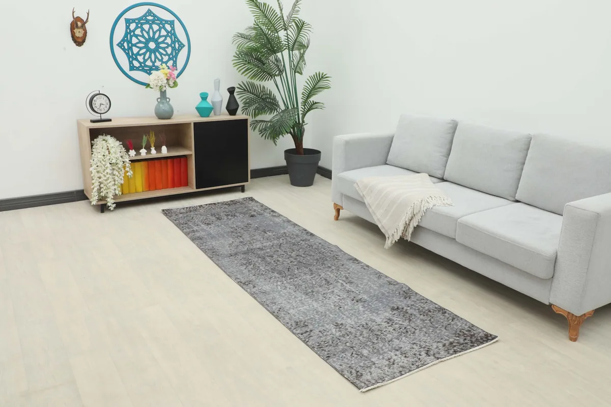 Runner rug in a living room setting next to a gray sofa and wooden cabinet