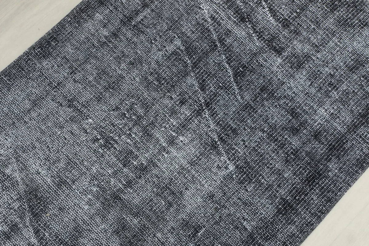 Detailed view of the rug's surface, showing the variations in charcoal and gray tones and distressed wool pile.