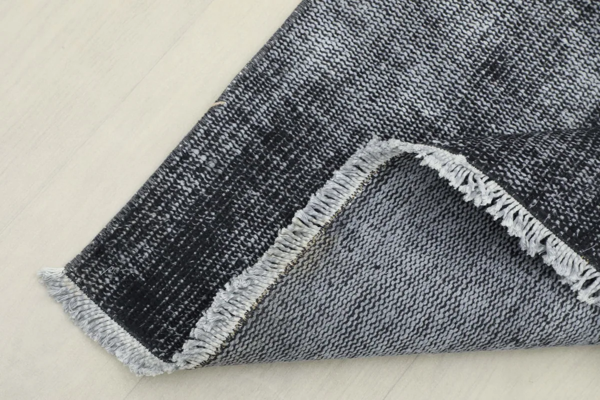Corner of the rug folded to show the hand-knotted cotton foundation and the reverse side.
