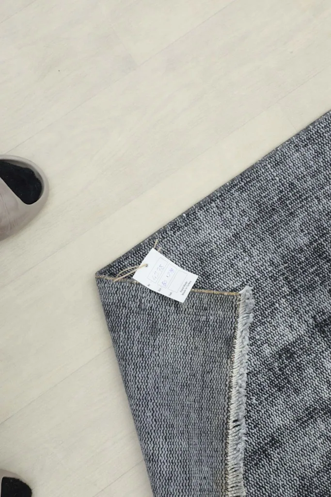 Overhead view of a corner of the rug with a tag, showing the natural light gray foundation.