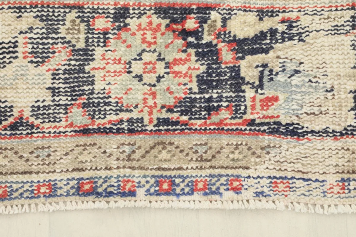 Close-up of the rug's border, revealing geometric and floral patterns in navy, beige, and red.
