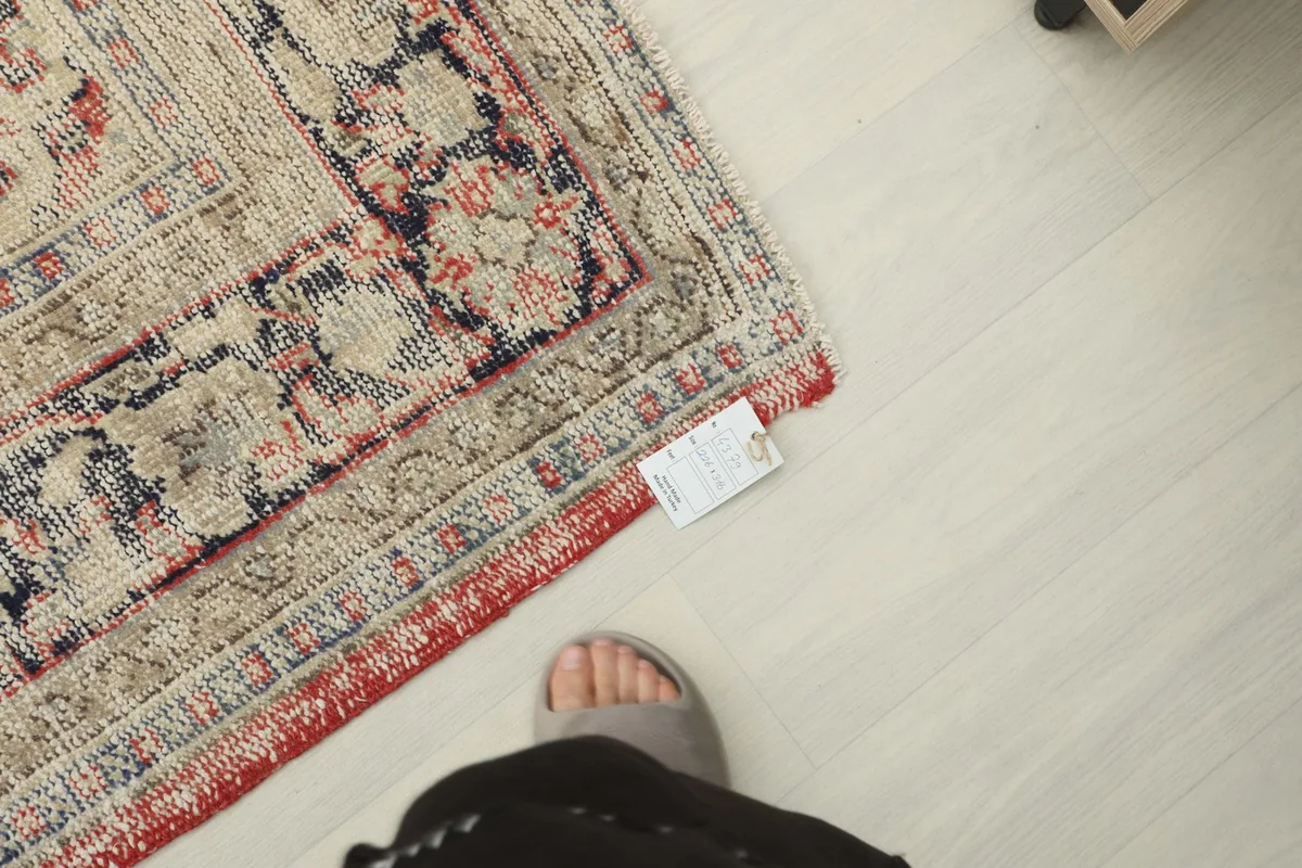 Edge of the rug with a size tag next to a foot for scale, showing the finished side.