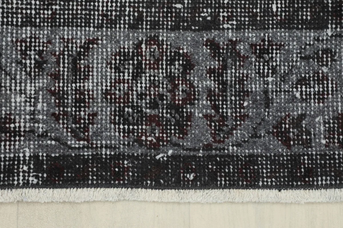 Detail of the rug's border, showing the intricate floral and geometric patterns in charcoal, gray, and red.