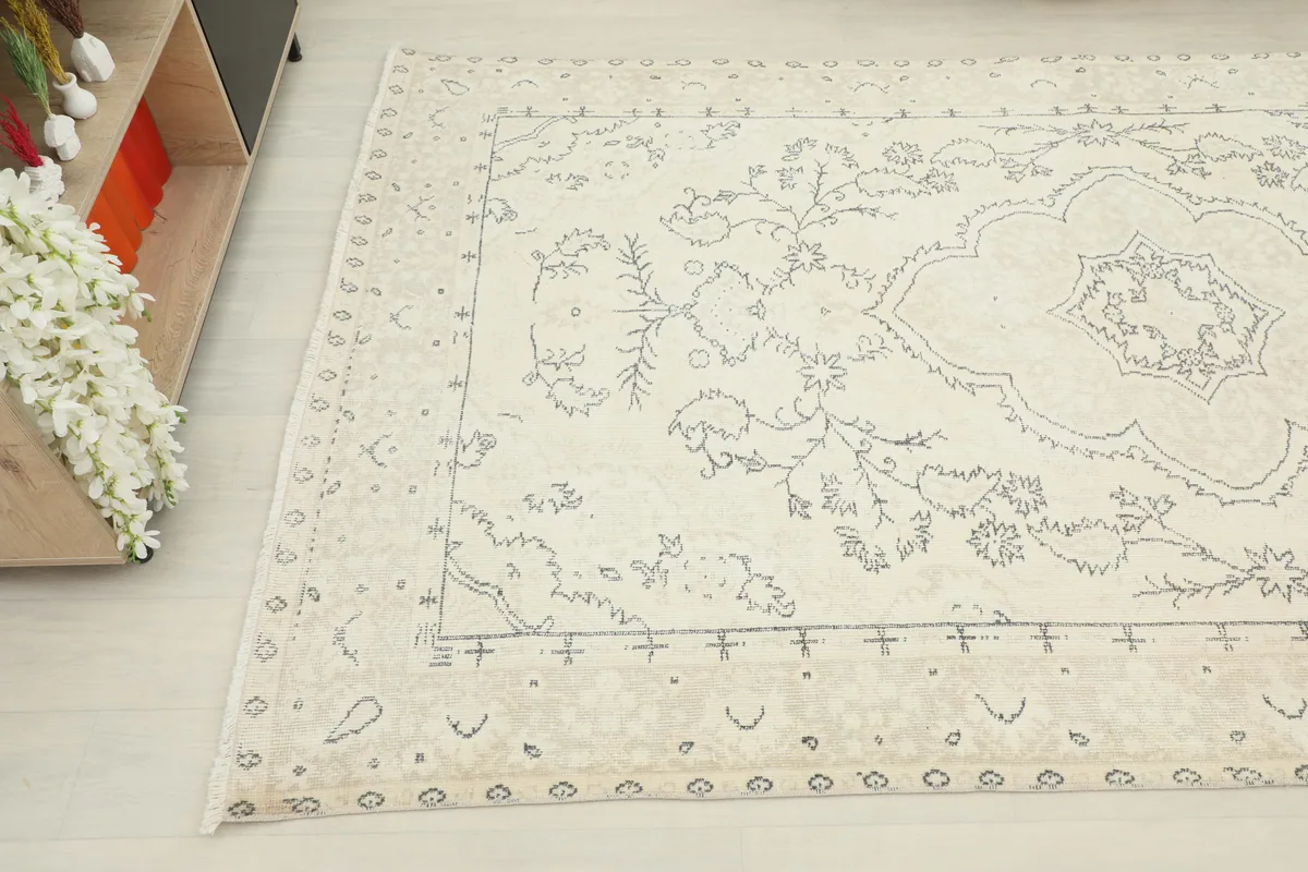An ivory rug's detail showing the subtle gray motifs and patina near the edge.