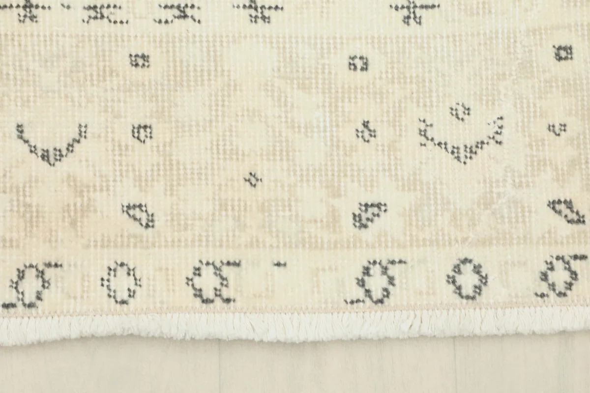 Detail of the rug's fringe and a section of its border with small gray motifs.
