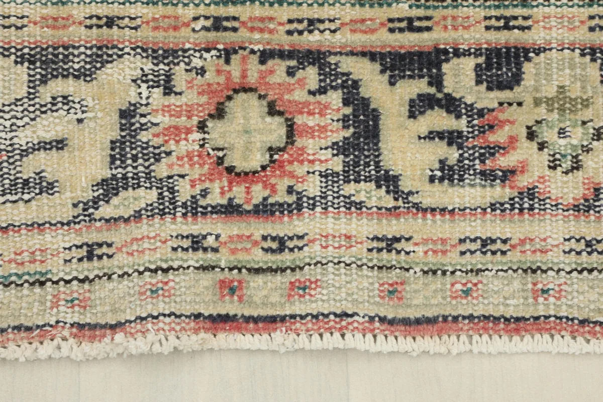Detailed shot of the rug's border, showcasing the navy, beige, and rose floral and geometric patterns.
