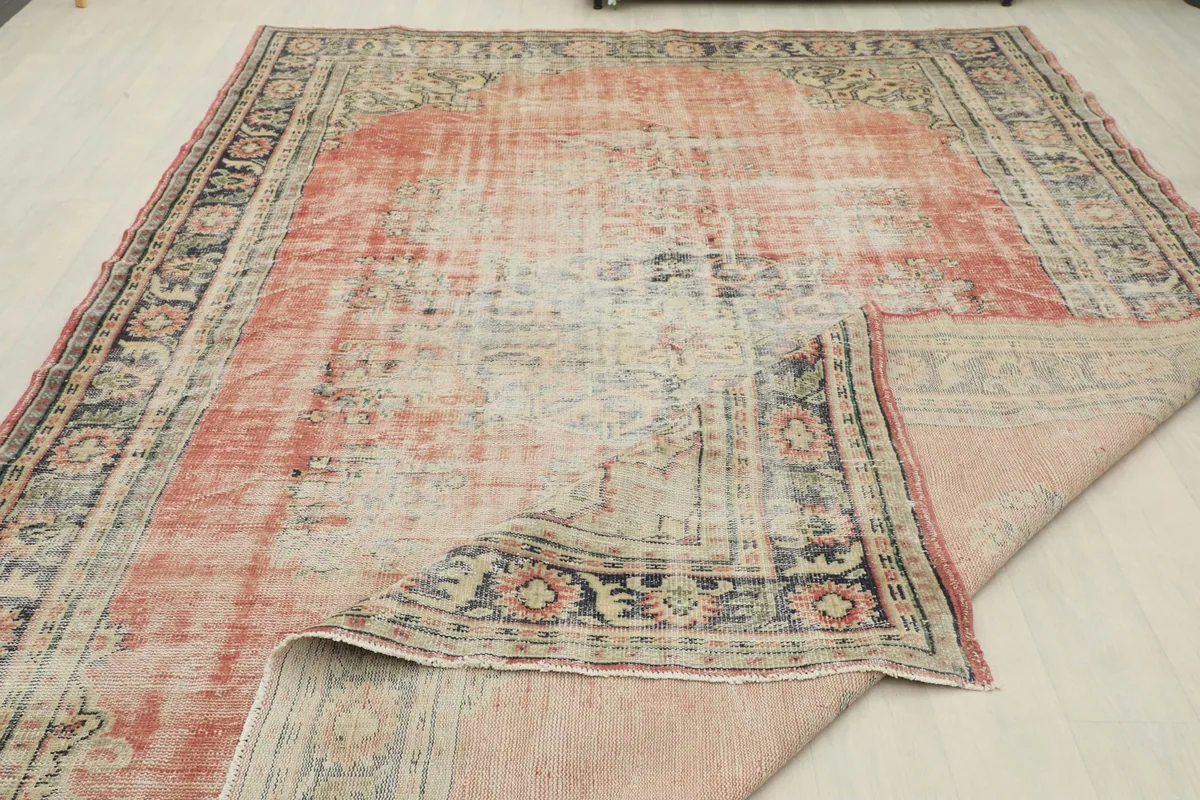 Overall view of the rug with a corner folded, showing the distressed surface and foundation.