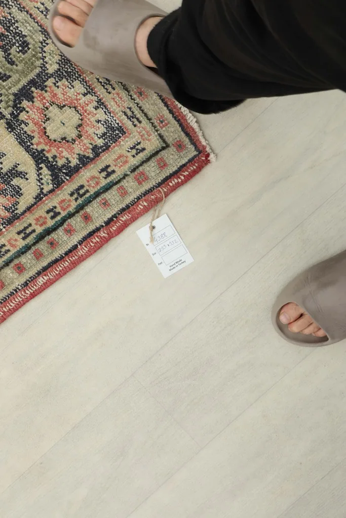 Foot next to the rug's edge, showing the scale and the small tag attached to the corner.