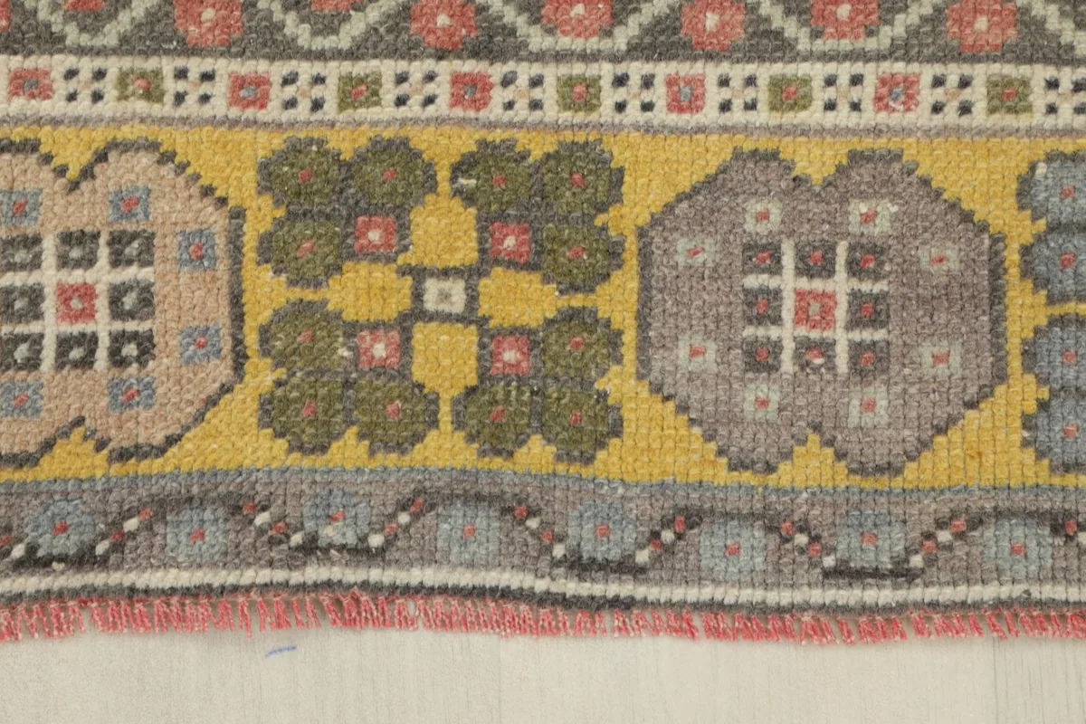 Close-up of the rug's border, showcasing the repeating floral and geometric elements in yellow, olive, and gray.