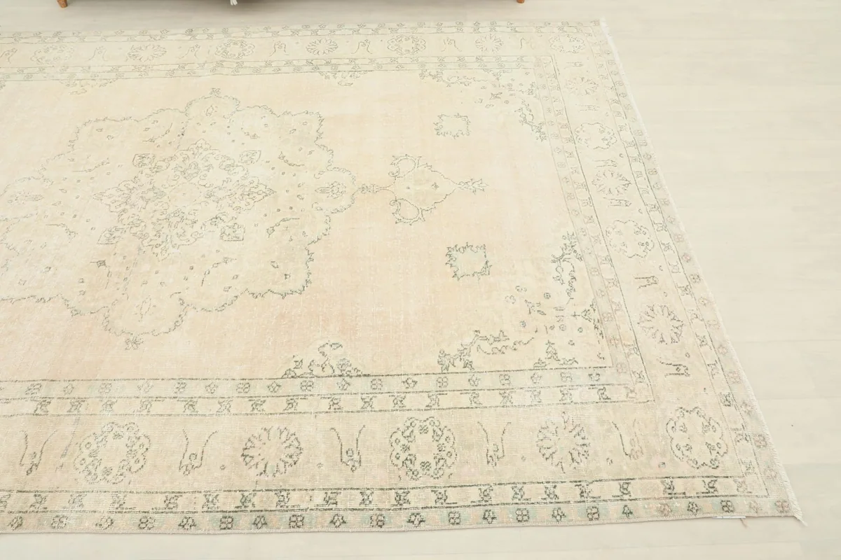 Close-up detail of the corner of the rug, showing the faded gray patterns against the beige field.