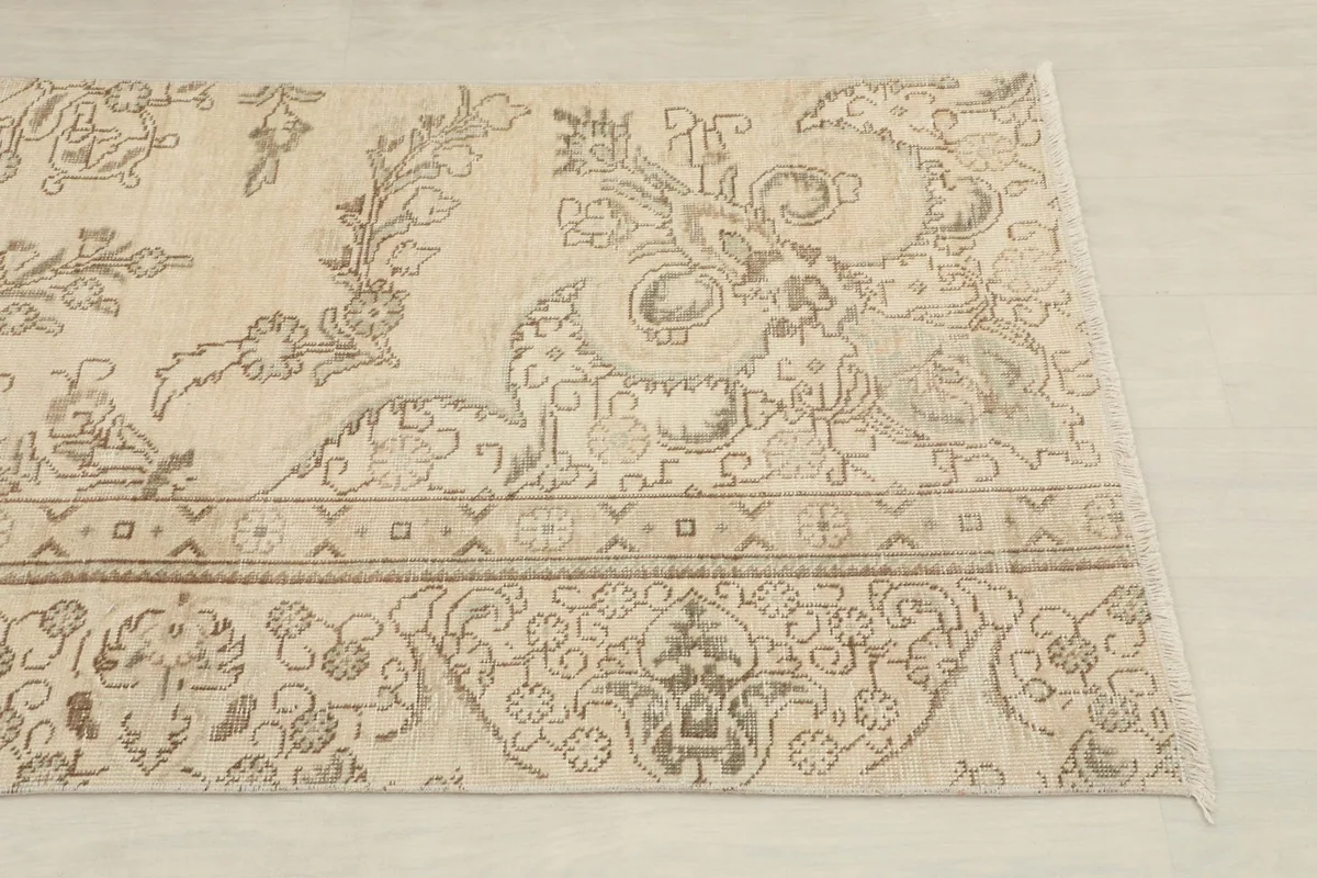 Close-up view of one end of the ivory runner rug, showing the distressed floral and geometric patterns.