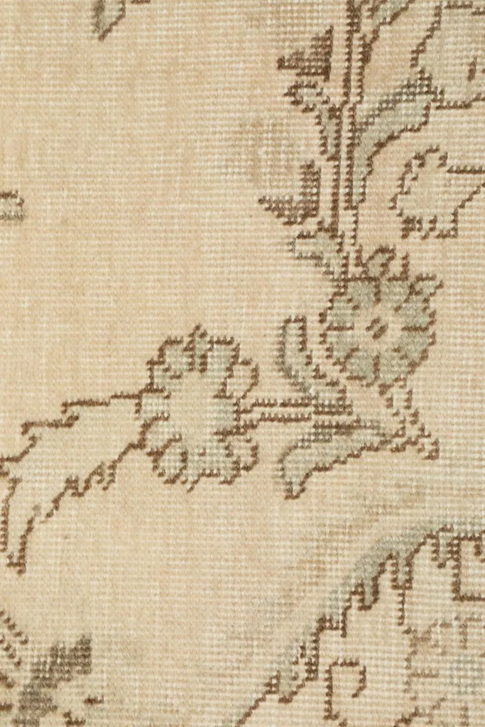 Macro shot of the low wool pile of the rug, showing the texture and subtle color variations in the ivory and tan.