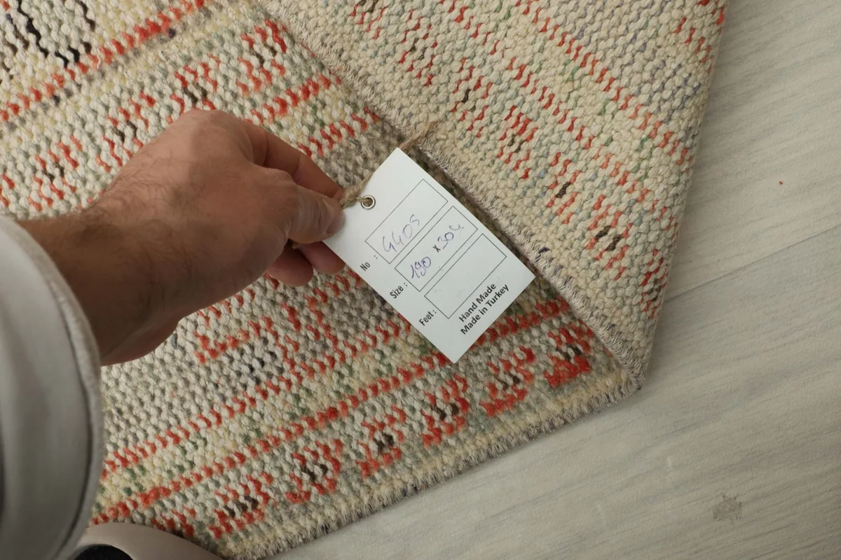 Hand holding a product tag against the back of the rug, showing the details of its origin and material
