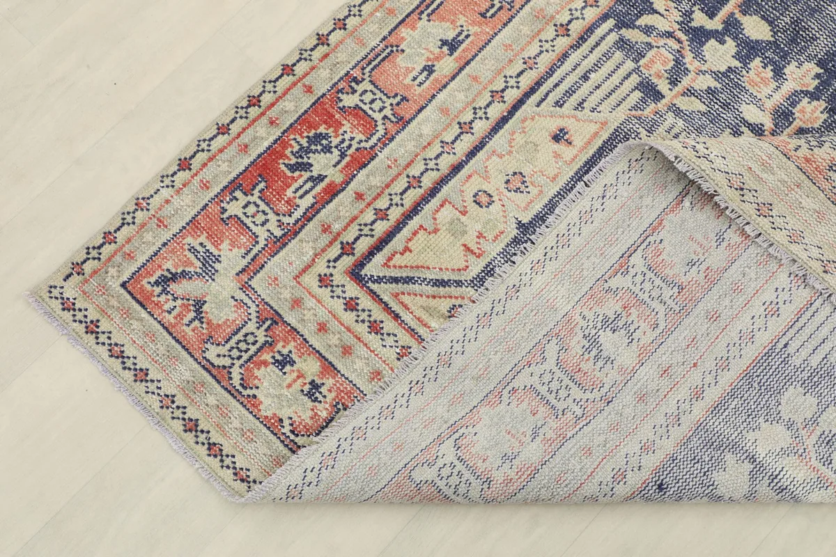 Corner of the rug folded back, showing the cotton foundation and the reverse side of the hand-knotted wool.