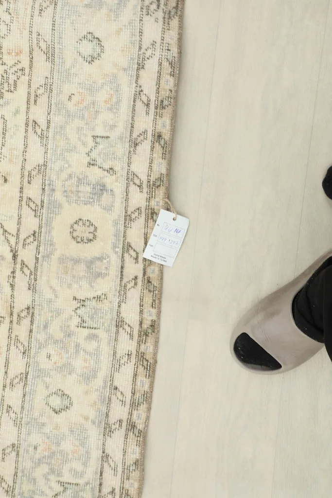 View of the rug with a size tag and a foot for scale, showing part of the border