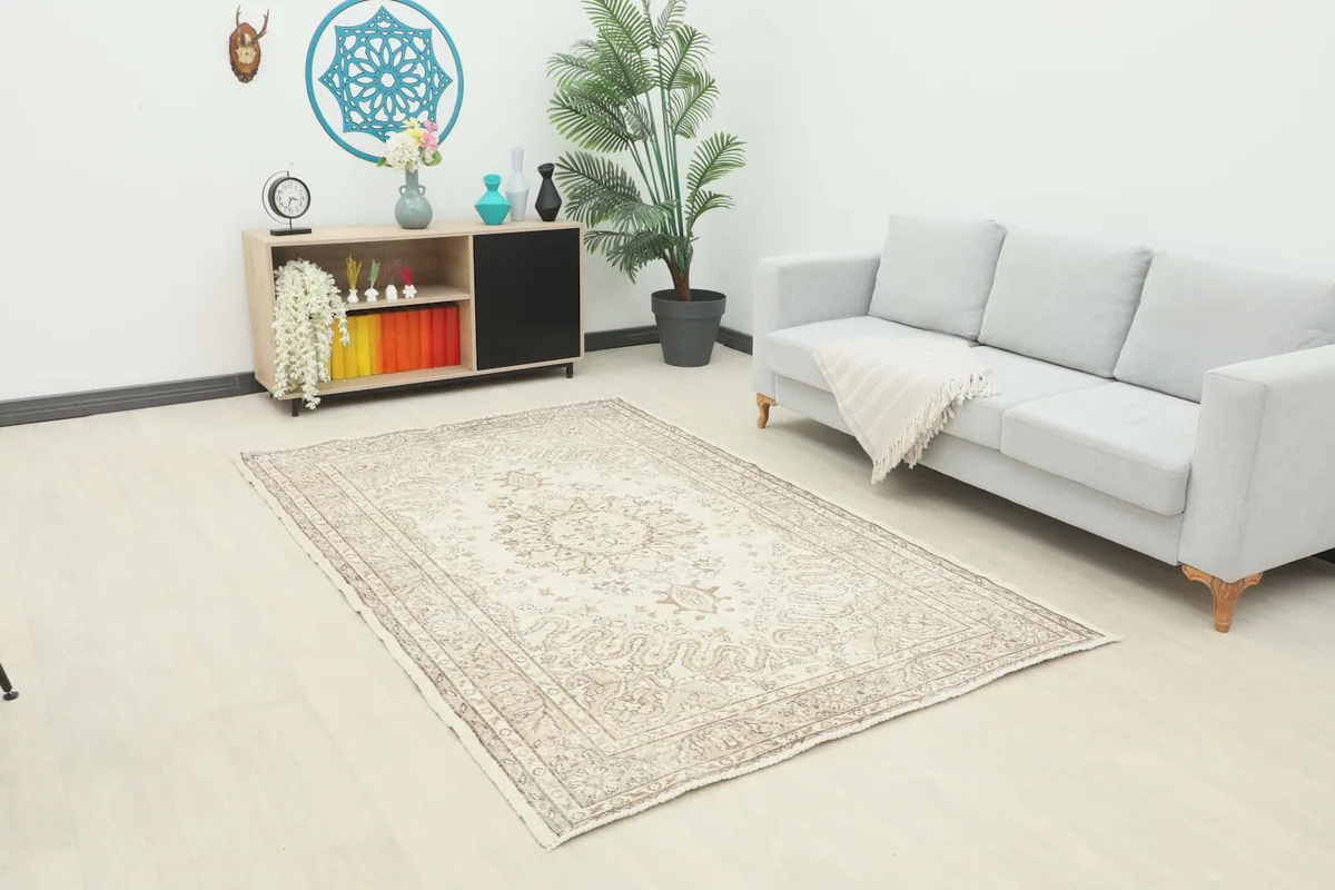 Ivory and beige vintage rug displayed in a living room setting with a sofa and cabinet.