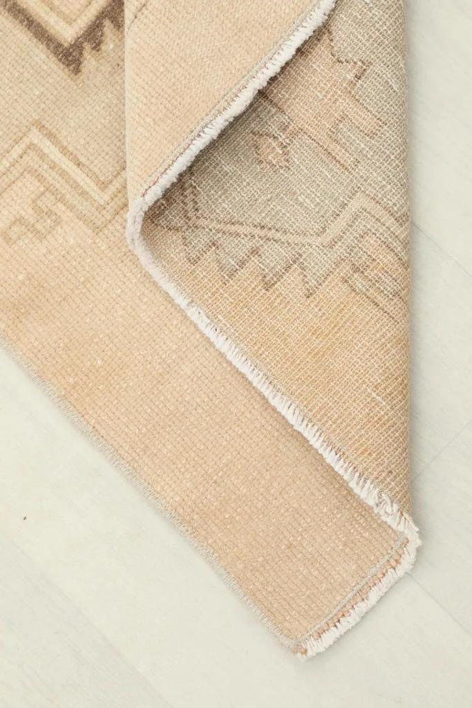 Corner of the runner rug folded back, revealing the cotton foundation and reverse side.