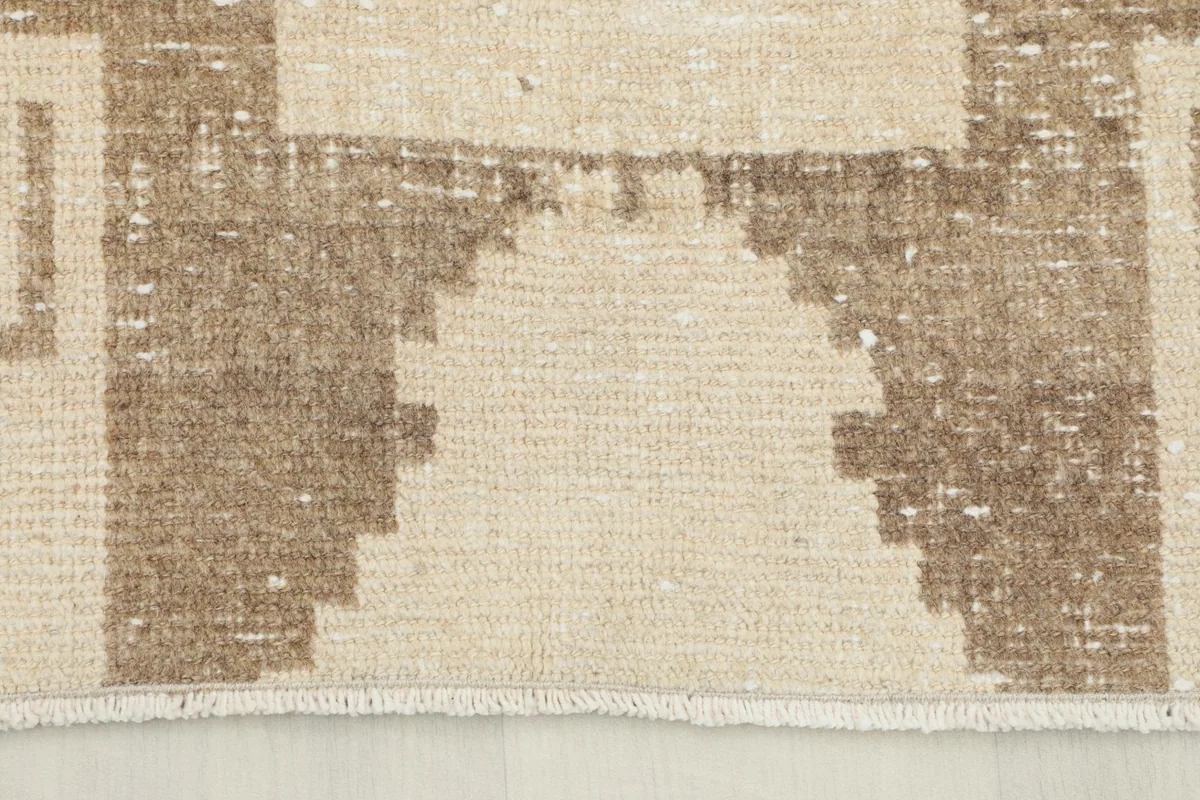 Close-up of the end of the runner rug, showing the fringe and faded brown pattern