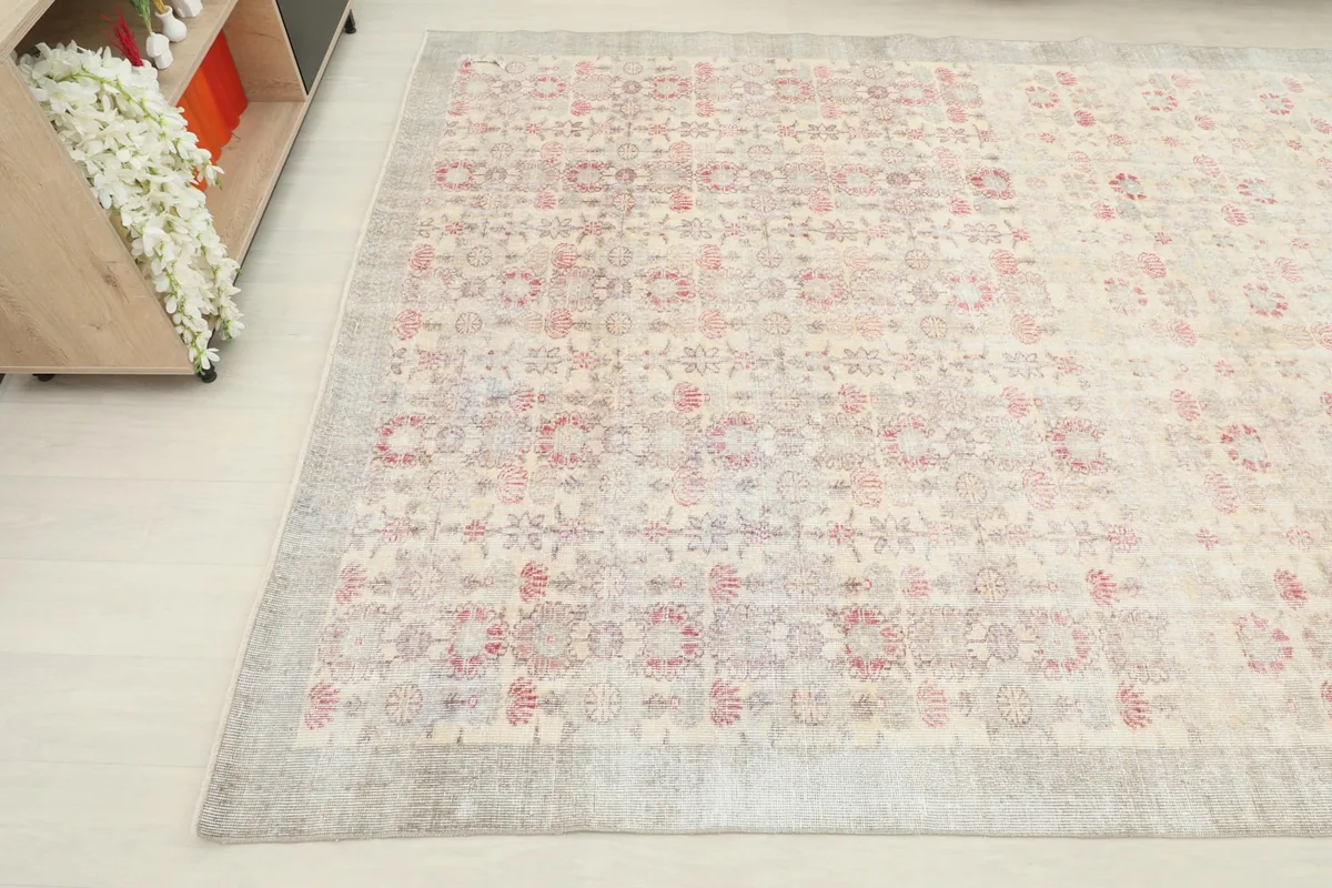 Angled view showing the rug's faded floral and geometric motifs across the cream field.
