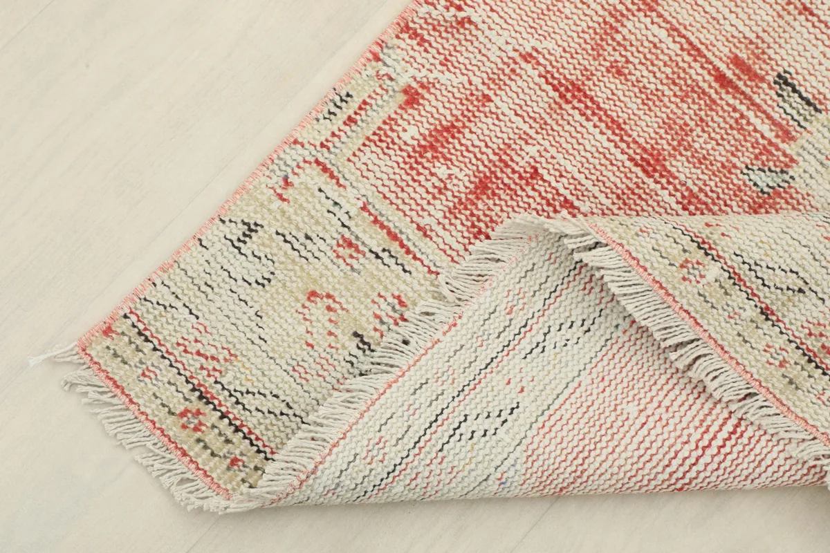 Corner of the runner rug folded back, showing the back of the hand-knotted cotton foundation