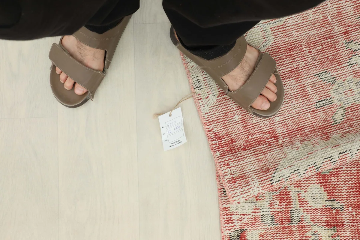 Feet in sandals next to the rug and its product tag, for scale reference