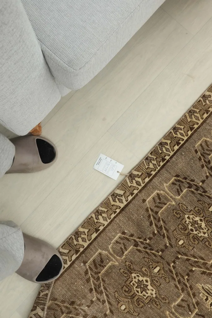 Overhead view showing the rug's border, a tag, and feet in slippers for scale.