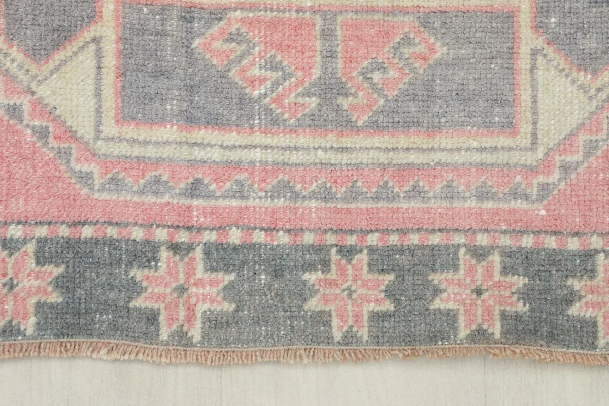 Close-up of the lower border and fringe of the rug, featuring gray with rose star motifs