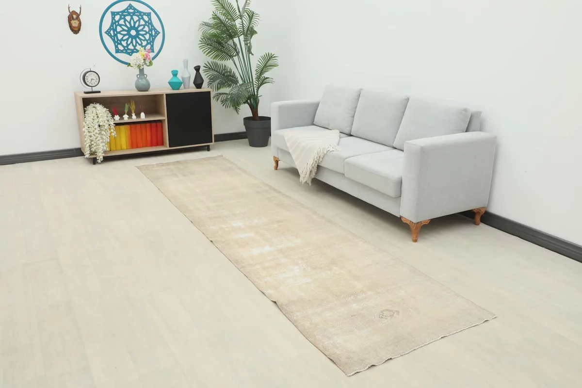 Vintage beige runner rug placed in a living room hallway next to a gray sofa and a small cabinet.