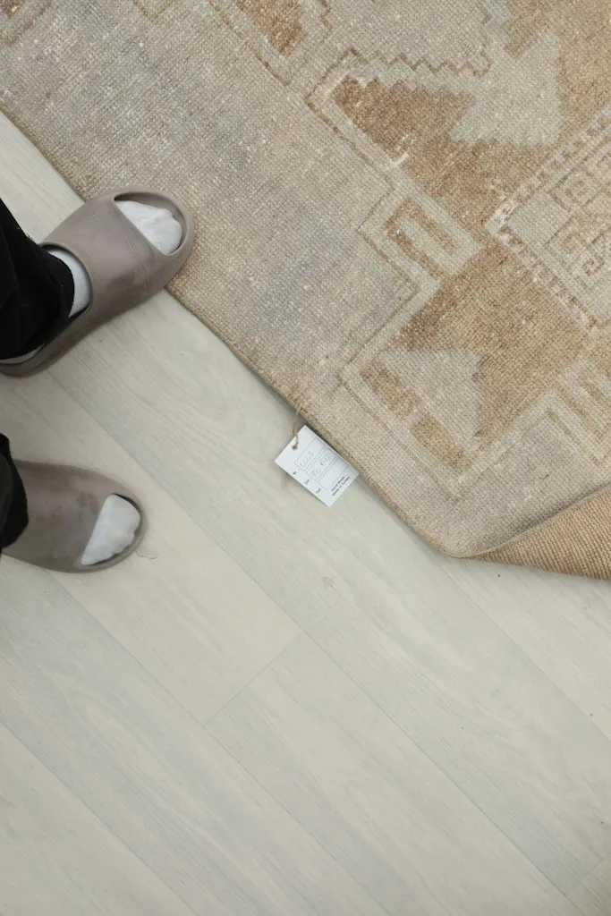 Human feet in slippers next to the rug, showing scale and the small tag attached
