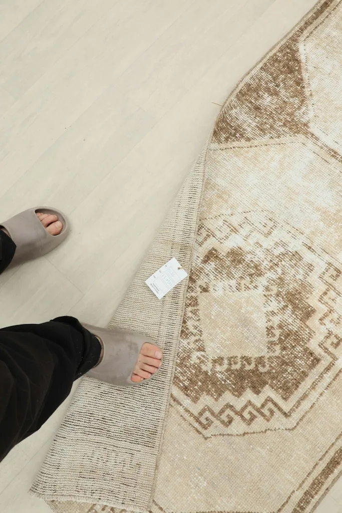 Foot next to the folded rug, indicating scale and showing the label on the rug's underside
