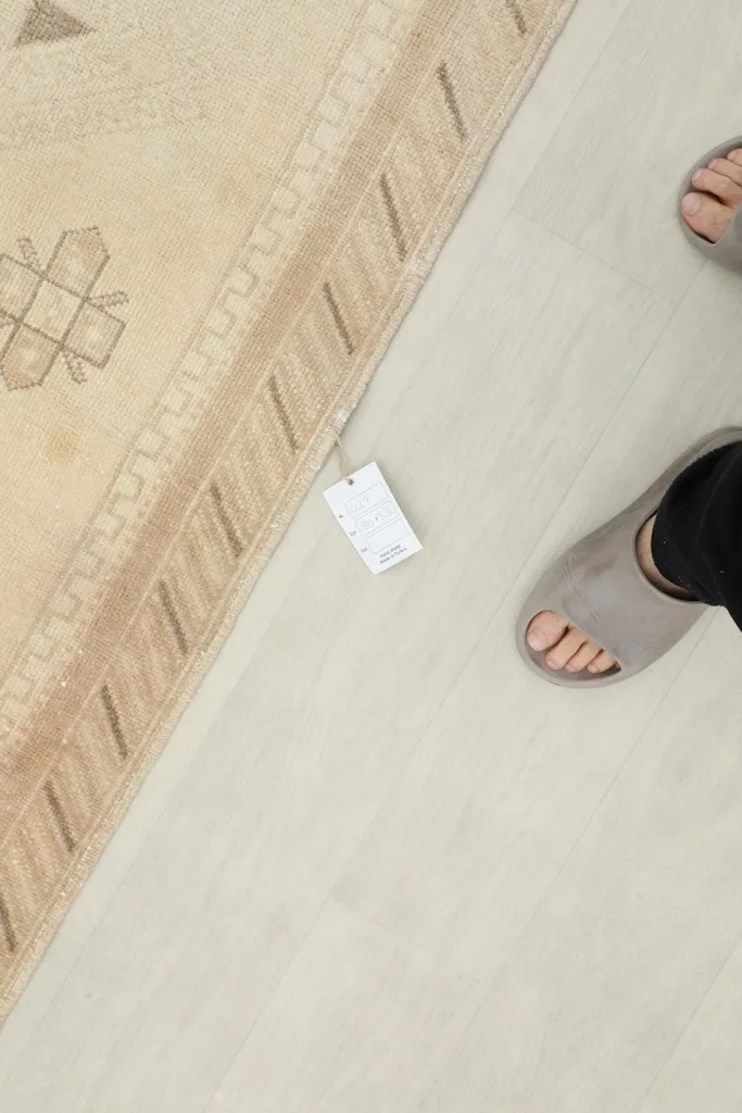 Close-up of the rug's border next to feet, showing the texture and a product tag.