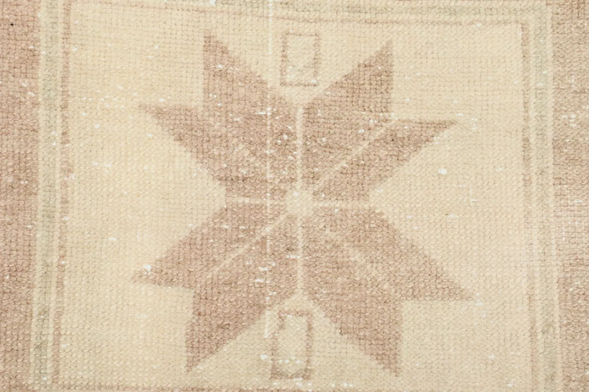 Close-up of a faded geometric pattern, showing the wool pile texture and slight variations in color.