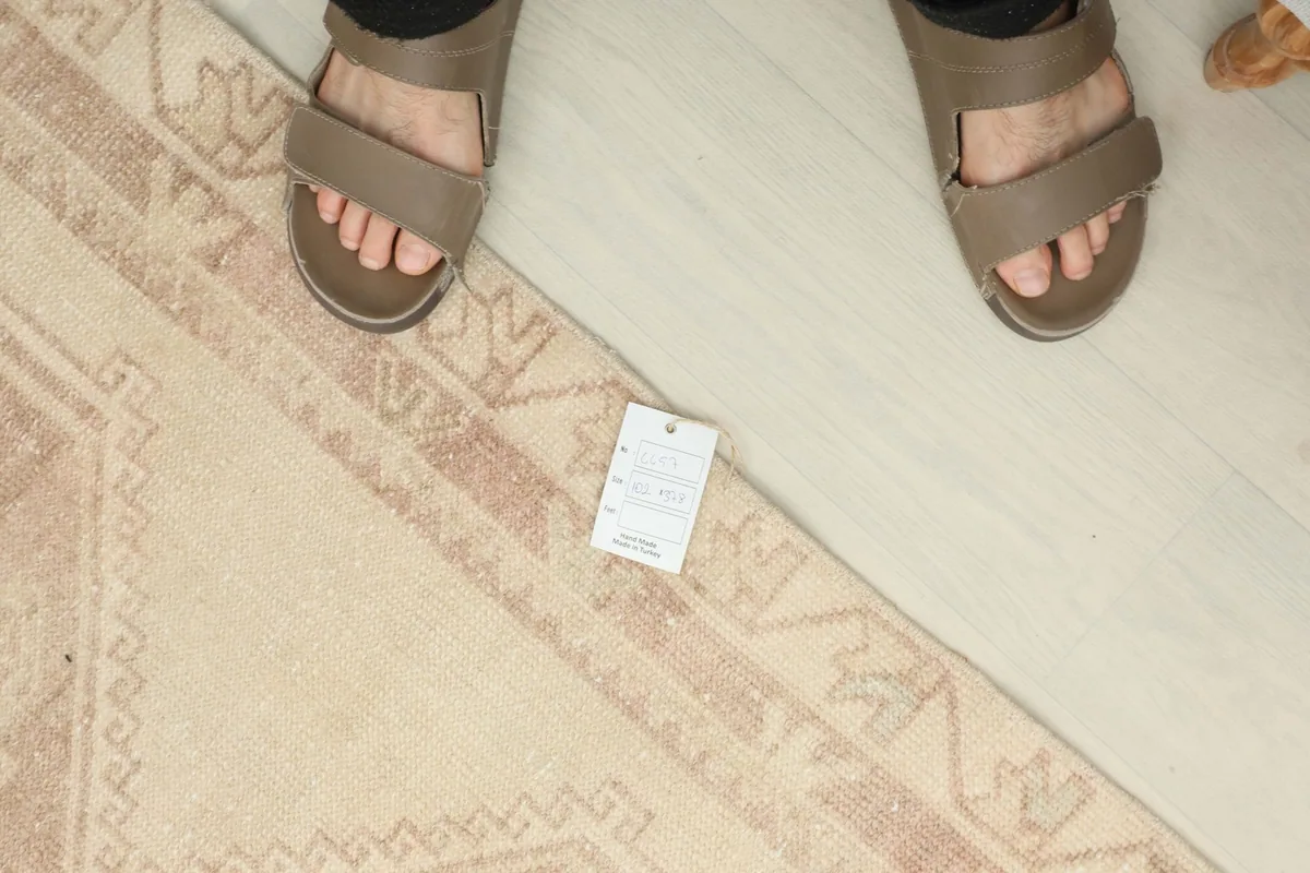 Overhead view of a person's feet on the rug, next to a product tag for scale and texture reference.
